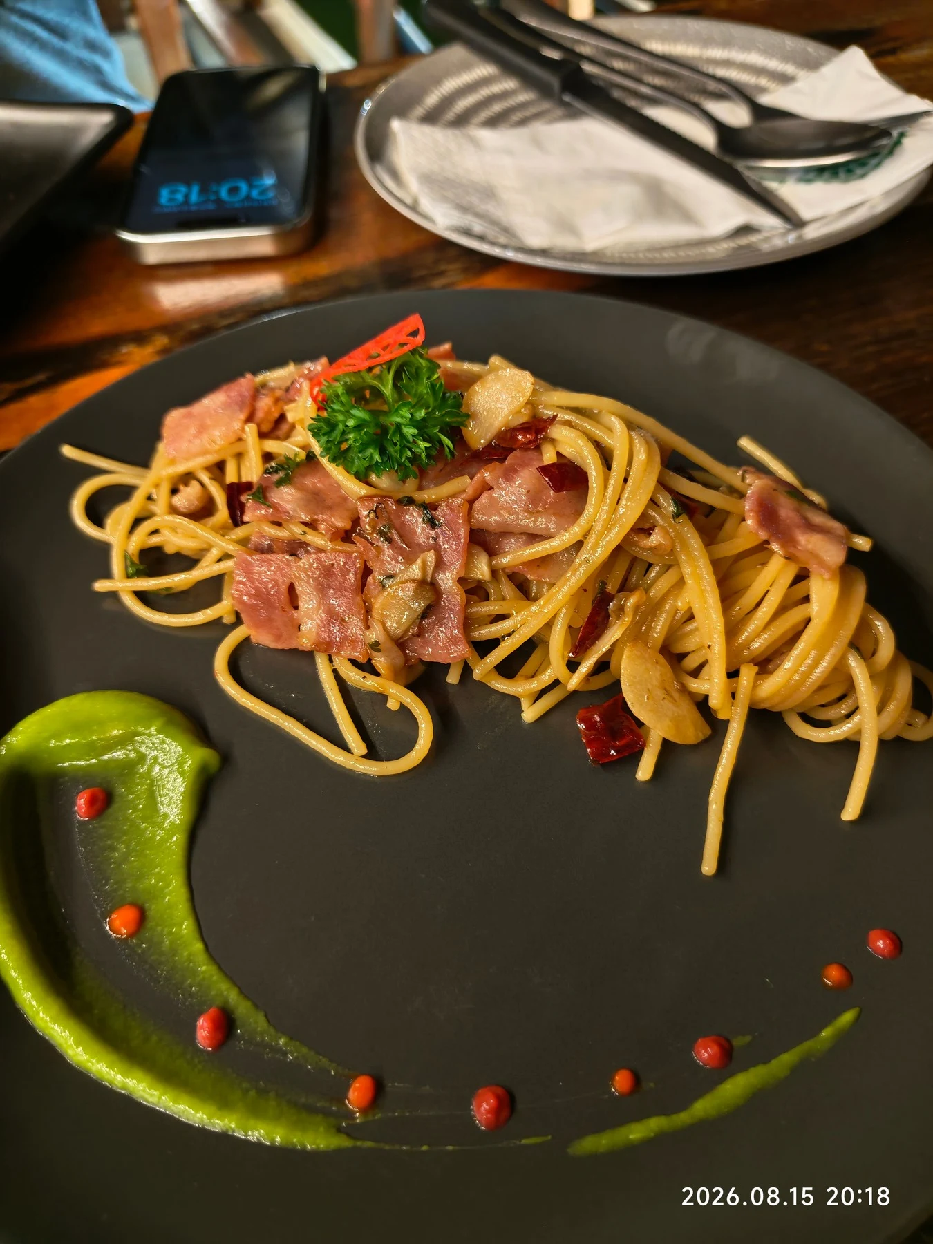 Spaghetti con carne a fette, aglio, peperoncino, prezzemolo e una salsa verde su un piatto nero